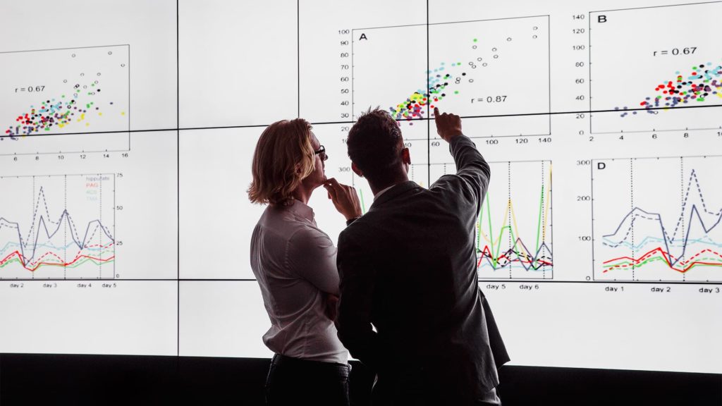 Two men looking at graphs on a wall screen